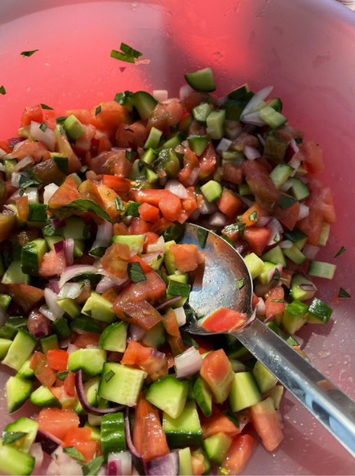 Bowl of chopped cucumber, tomato, red onion, and herbs with a metal spoon