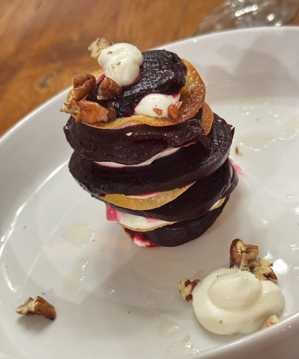 Stacked beet and golden chip slices layered with cream and chopped walnuts on a white plate