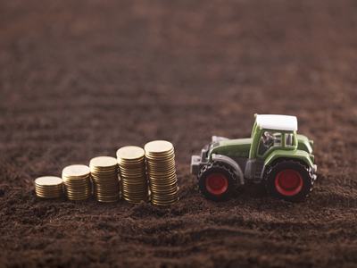 Toy tractor on soil beside ascending stacks of gold coins