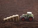 Toy tractor on soil beside ascending stacks of gold coins