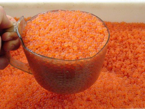 Clear measuring cup filled with orange salmon roe held over a tray of more roe