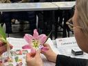 Person examining a pink lily at a table; name tag reads "Catherine Sch"