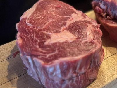 Raw ribeye steak with visible marbling resting on a wooden cutting board