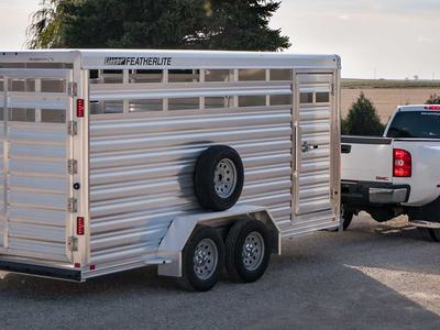 Aluminum Featherlite livestock trailer hitched to white pickup truck on gravel road