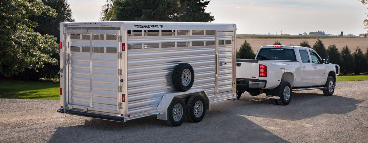 Aluminum Featherlite livestock trailer hitched to white pickup truck on gravel road
