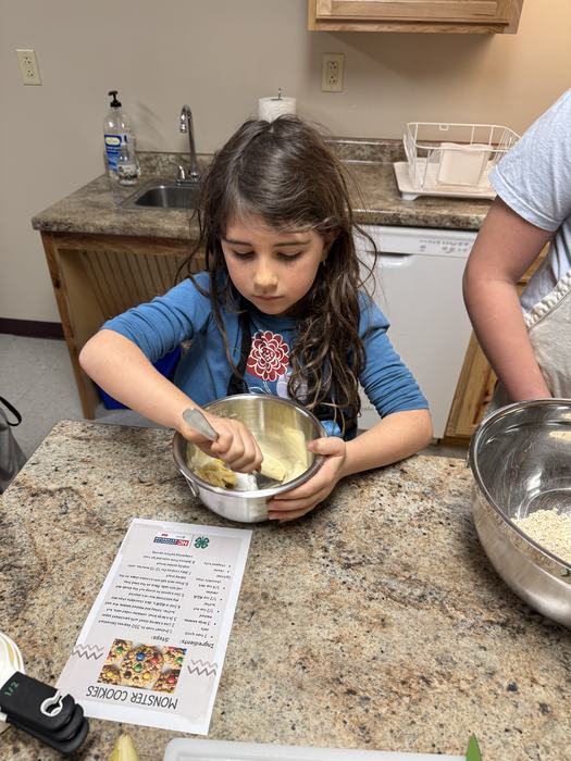A girl mixes ingredients in a bowl while following a recipe.