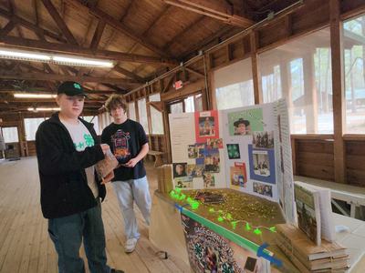 Two teenage boys standing by a 4-H display table in a wooden pavilion labeled GAGE GARRISON
