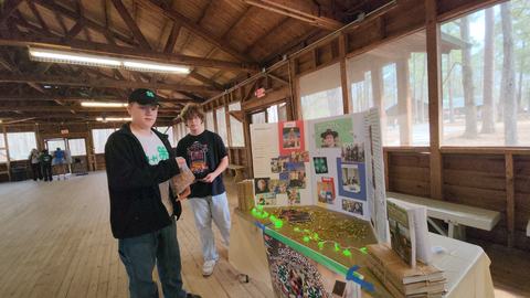 Two teenage boys standing by a 4-H display table in a wooden pavilion labeled GAGE GARRISON