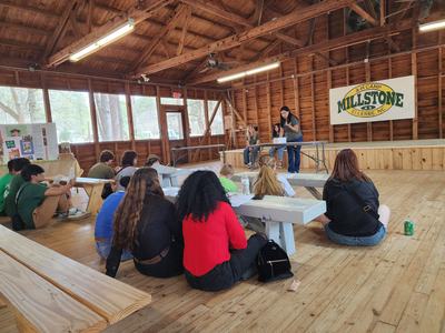 Group of people seated on benches listening to a presenter at Millstone camp pavilion