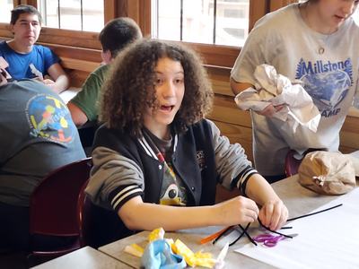 Curly-haired teen at table working with pipe cleaners and scissors during a craft session