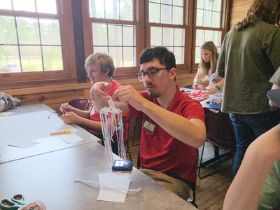 Young man in red shirt crafting a yarn tassel with hanging strands at a table