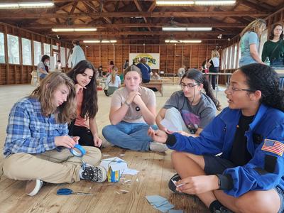 Group of five teens sitting on a cabin floor making crafts with tape, paper, and scissors