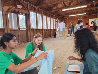 Three girls sitting on a wooden floor assembling light-blue fabric and a small box