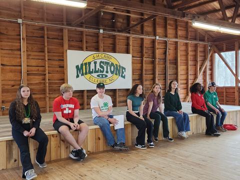 Youth seated on a wooden stage under sign "MILLSTONE 4-H CAMP ELLERBE, NC"