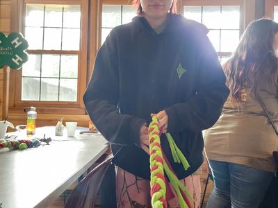 Person wearing baseball cap braiding neon green and pink paracord rope indoors