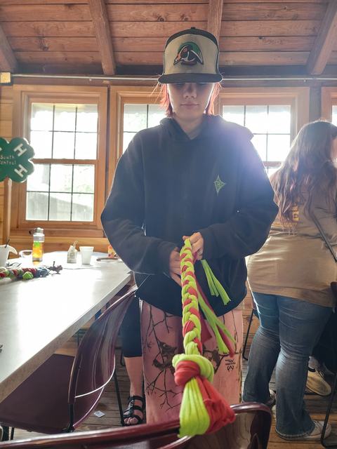 Person wearing baseball cap braiding neon green and pink paracord rope indoors