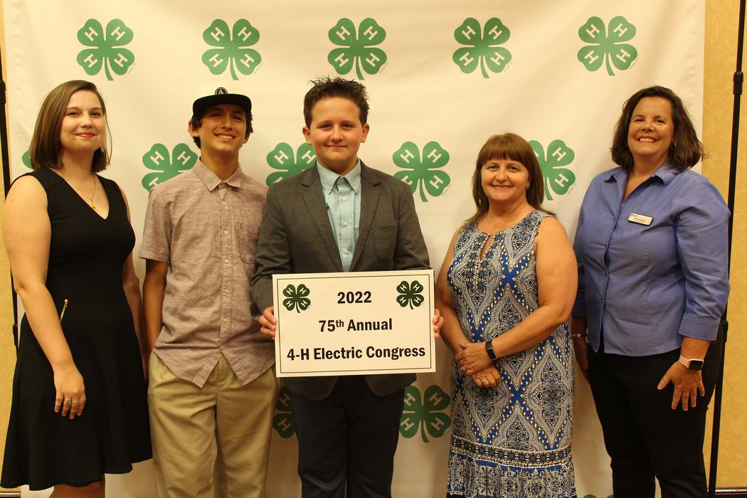 Five people pose holding a sign reading "2022 75th Annual 4-H Electric Congress"