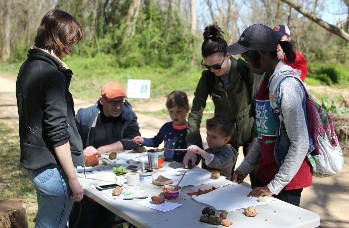 Group of adults and children painting rocks on a folding table outdoors