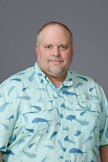 Man wearing a light blue button-up shirt with blue fish pattern against gray background