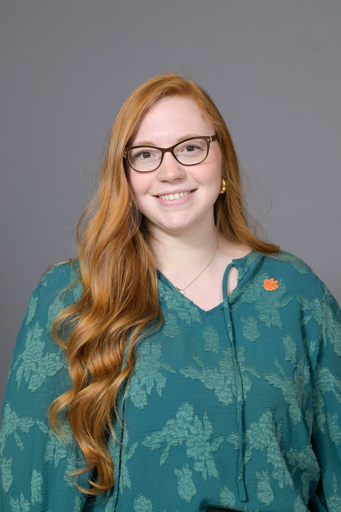 Woman with long red hair and glasses wearing teal blouse and orange paw pin