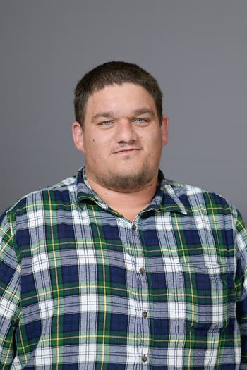Man wearing green-and-blue plaid shirt facing camera against gray background
