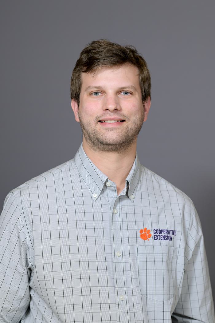 Male headshot wearing checked shirt embroidered "COOPERATIVE EXTENSION" with orange paw