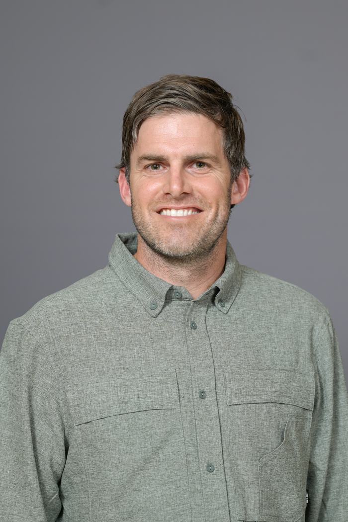 Head-and-shoulders portrait of a man wearing a green button-up shirt on a gray background