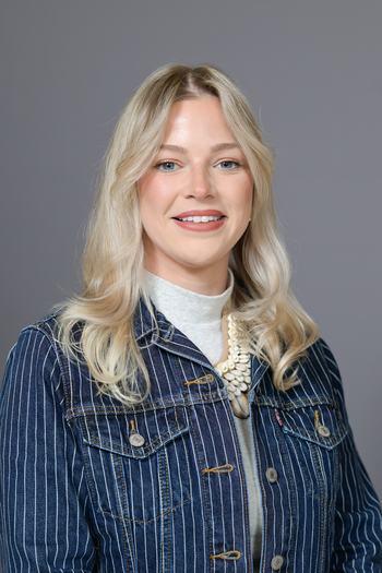 Young woman smiling, wearing striped denim jacket and shell necklace
