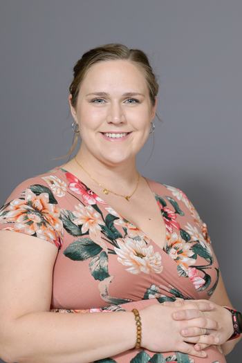 Woman in floral dress with hands clasped against gray background