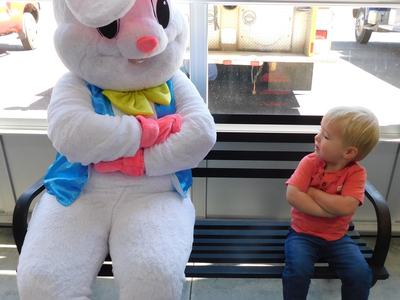 Toddler with arms crossed on bench looking at person in Easter bunny costume with arms crossed