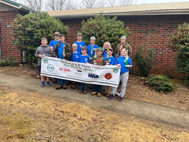 4-H Young guns pose with a sponsorship banner.
