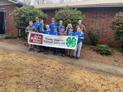 4-H Young guns pose with a sponsorship banner.