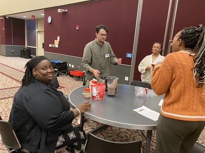 Four people around a table with a blender making drinks in a conference room