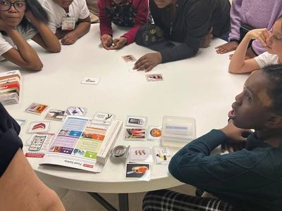 Children and teens gathered around a table sorting picture cards and a booklet.