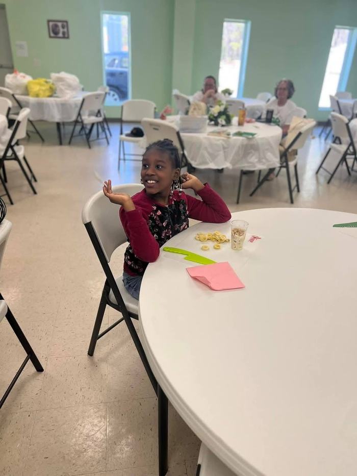 A girl smiles at a table with food in front of her.