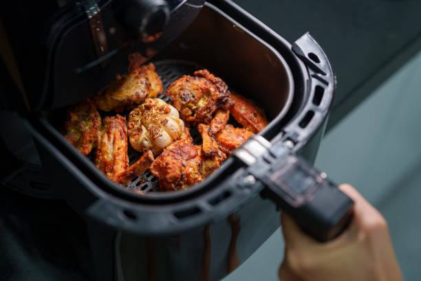 A woman is using an air fryer to prepare grilled chicken in her kitchen, focusing on a healthier cooking method with minimal oil.