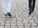 Two people's lower legs and shoes walking on cobblestone pavement