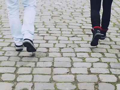 Two people's lower legs and shoes walking on cobblestone pavement