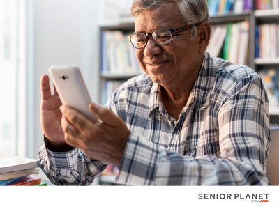 Older man holding smartphone in front of bookshelves; text "SENIOR PLANET FROM AARP"