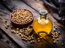 Close up view of a glass bottle filled with soy oil shot on rustic wooden table. A bowl with dried soybeand complete the composition Plant-based nutrition concept. High resolution 42Mp studio digital capture taken with Sony A7rII and Sony FE 90mm f2.8 mac