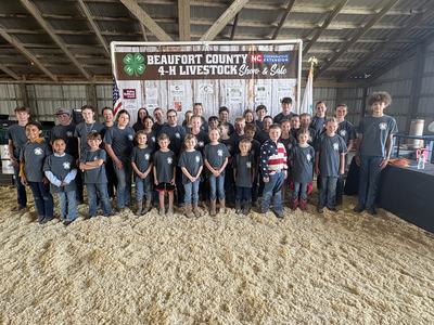 Children and teens standing in a barn under sign "Beaufort County 4-H Livestock Show & Sale"