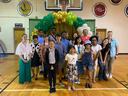 Group of students and adults posing in a gym under a green and gold balloon arch