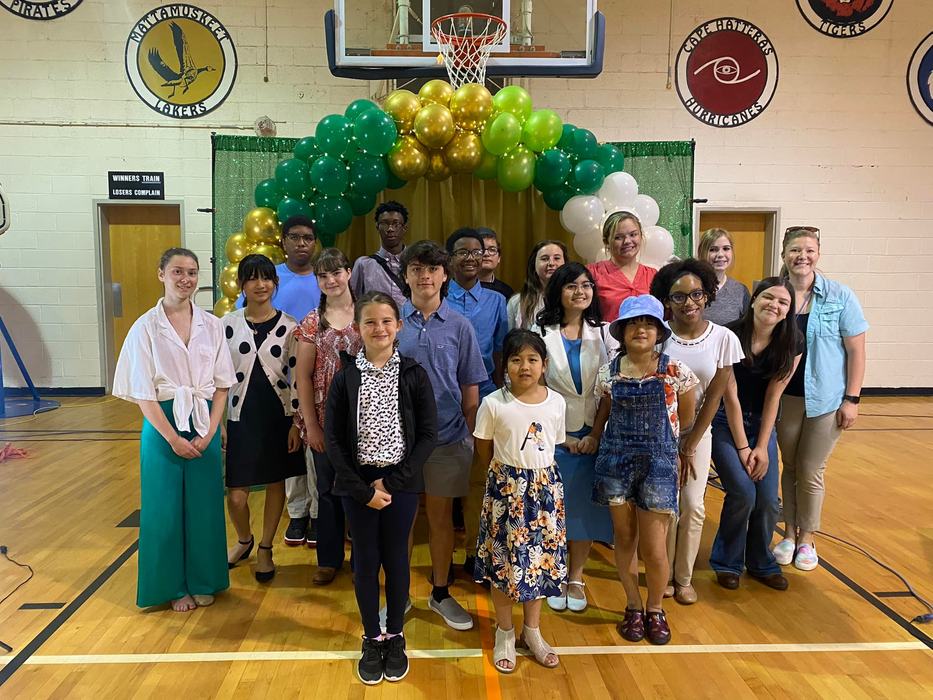 Group of students and adults posing in a gym under a green and gold balloon arch