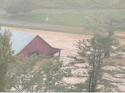 Red barn partially submerged by muddy floodwaters amid trees