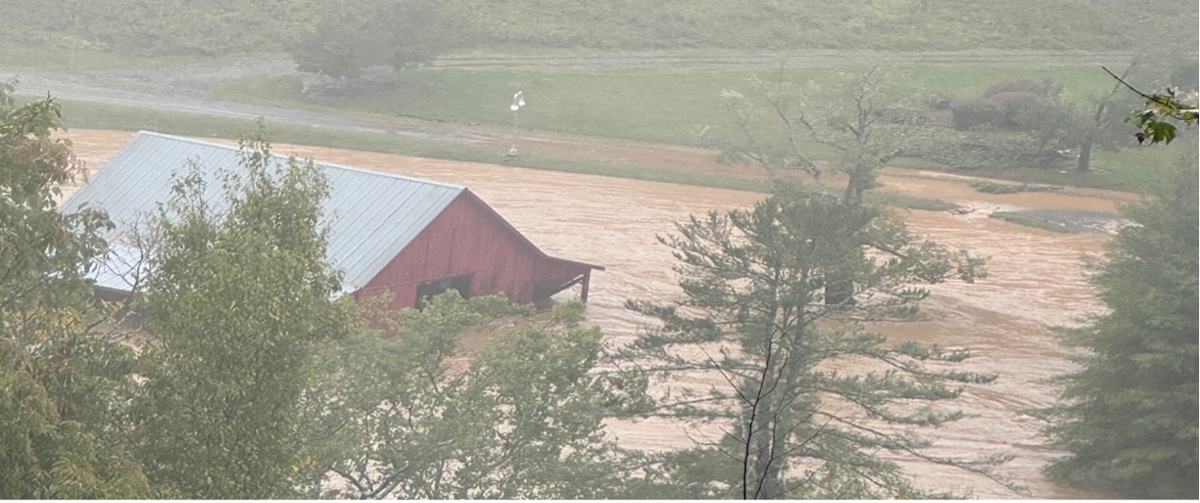 Red barn partially submerged by muddy floodwaters amid trees