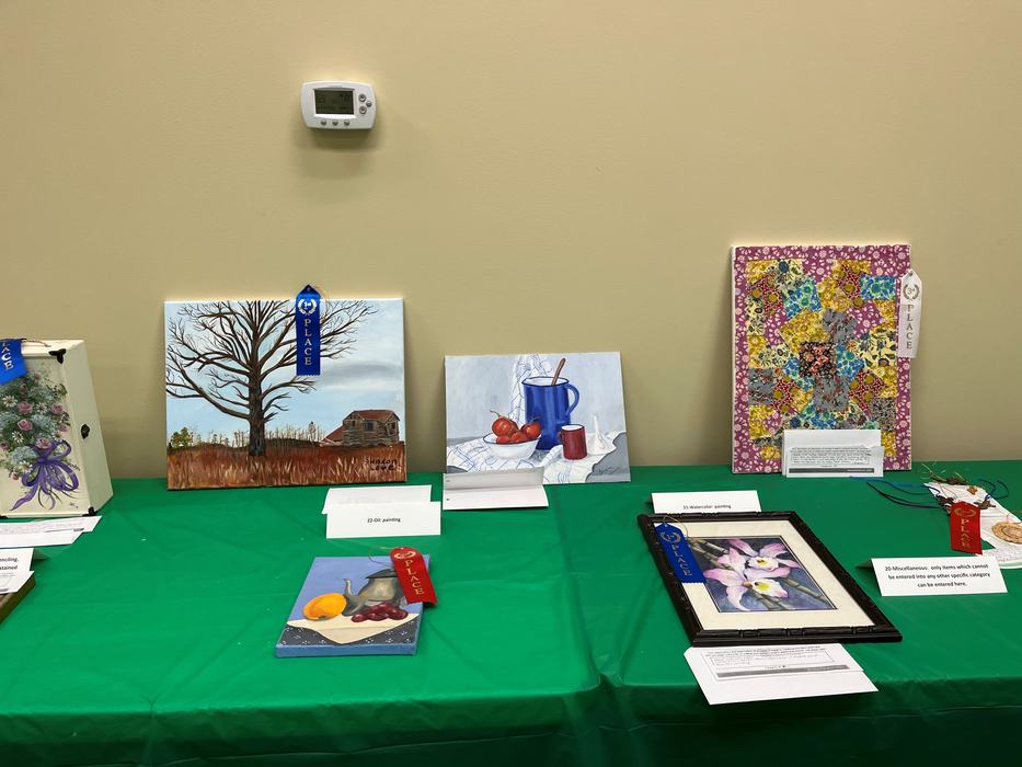 Table with several small paintings and award ribbons displayed on a green tablecloth