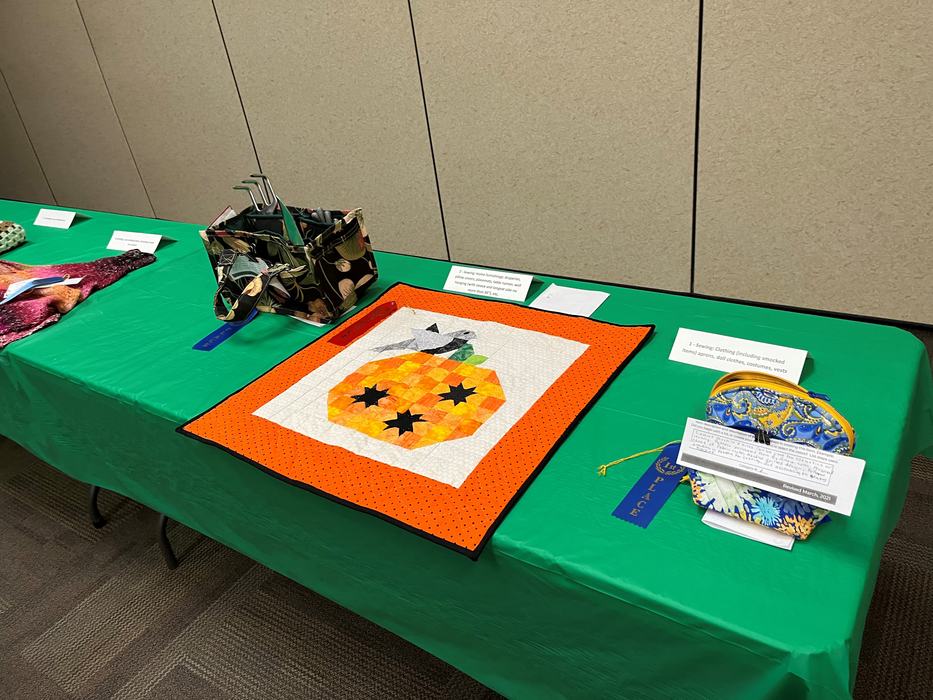 Green table with pumpkin quilted wall hanging, fabric pouches and award ribbons