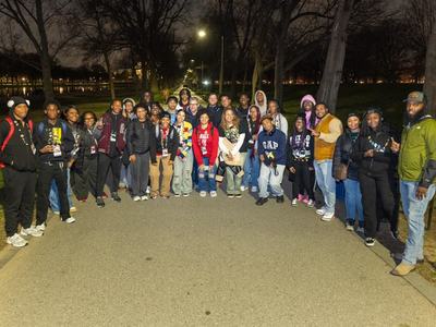 Large group of people standing on a park path at night, trees and lights in background