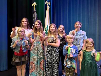 Children on stage holding ribbons and medals in front of US and 4‑H flags
