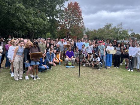 Large group of people on a lawn, several holding honeycomb frames from beehives
